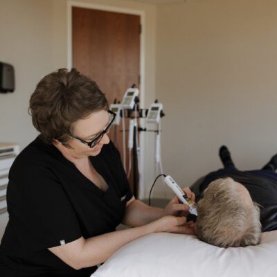 Danielle Adair, a licensed acupuncturist at Muscle Restoration Therapy in Fort Collins, performing electro-acupuncture therapy on a client’s ear for pain relief and energy balance.